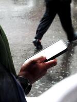 hand holding a smartphone with white blank screen on outdoor area during the rainy days photo