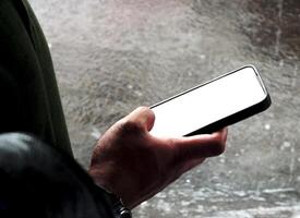hand holding a smartphone with white blank screen on outdoor area during the rainy days photo