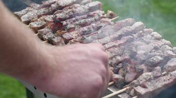 young man grilling meat kebabs on coals, ARROSTICINI - typical southern Italian cuisine, a luxurious picnic on the terrace near the house in summer,aromatic smoke rises from the barbecue, video
