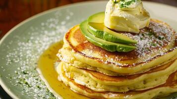 A stack of fluffy pancakes with a dollop of avocado oil butter and some sliced avocado on top highlighting the ingredients use in both sweet and savory dishes photo