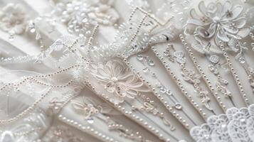 A dainty white and silver hand fan with a floral pattern embellished with shimmering beads and a delicate fringe photo