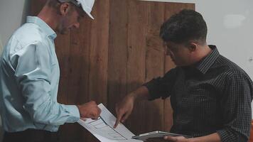 Teamwork men in construction site, Two civil engineer or professional foreman in safety helmet hard hat using blueprint in digital tablet working while standing at industrial factory, teamwork concept video