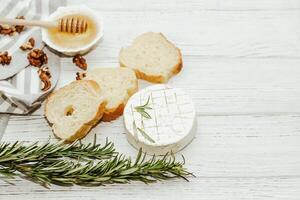Round cheese in camembert mold with a sprig of rosemary, honey and nuts on the table. photo
