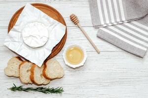 Camembert cheese with baguette croutons and a sprig of rosemary with honey on the table. photo