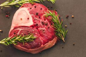 Fresh piece of meat large beef steak on the bone ossobuco with a sprig of rosemary on a black background. photo