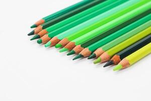 Multi-colored pencils lie on a white table, the green range of colors photo