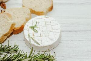 Round cheese in camembert mold with a sprig of rosemary, honey and nuts on the table. photo