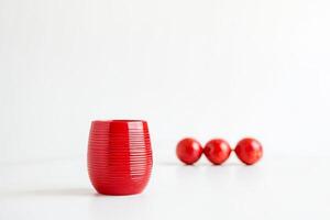 Red ceramic vase with three red round objects in the background on a white surface photo
