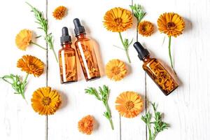 Calendula Oil Bottles With Flowers On White Wooden Background photo