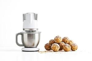 White stand mixer with a bowl full of dough next to a pile of eclairs photo