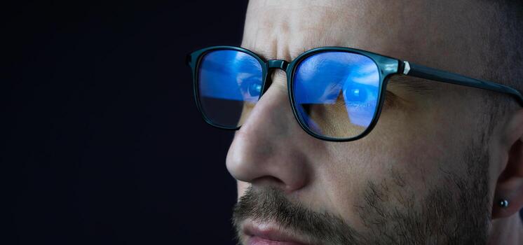 Focused eyes of a young man in glasses looking at a computer. Work online, work at the computer until late in the evening, workaholic. Banner. Close-up. Copy space. photo