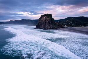 Beautiful iconic Lion Rock and breaking wave on Piha beach in the evening at Auckland, New Zealand photo