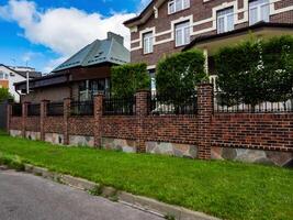 combined brick and wrought iron fence with brick pillars on a strip foundation near a country house photo