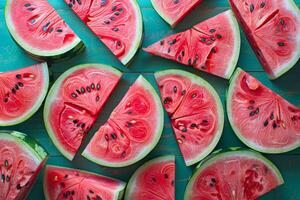 Top view of fresh watermelon slices arranged on a turquoise wooden background. The vibrant red flesh contrasts beautifully with the green rind and black seeds, creating a colorful photo