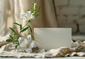 White lily with green leaves and blank card on beige fabric, illuminated by soft natural light photo