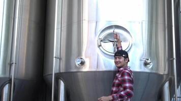 Asian worker checking the pump of a brewing tank while smiling at the camera, home brewing concept video