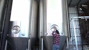 Asian worker checking the pump of a brewing tank while smiling at the camera, home brewing concept video