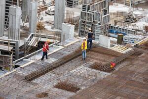 Aerial view of busy industrial under construction site workers working with cranes and excavators. Top view of precast concrete slap floor full of steel. Development high rise architecture building. photo