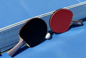 Two table tennis rackets and balls on a blue table with net. photo