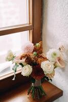 Bride bouquet stands on the windowsill in the room photo