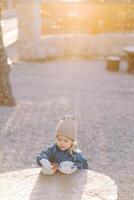 Little girl takes a piece of cucumber from a lunchbox while standing behind a large tree stump in the park photo