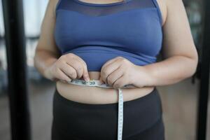 Obese Woman with fat belly in dieting concept. Overweight woman touching his fat belly and want to lose weight. Fat woman waist with centimeter Shape up healthy stomach muscle. photo