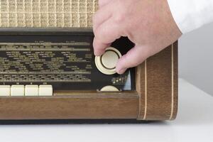 Real radio from the 50s - 60s. On a white table. Traces of time. The hand of a man on the radio dial sets the wave. Close-up photo