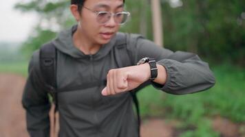 A young man was hiking and looked at his watch to see the time. Move forward with a happy smile and determination, go hiking, relax in the forest. video