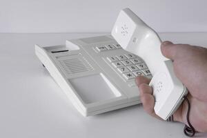 Desk phone 80s, 90s. Push-button dialing. White. Isolated on white table with a hand of man photo