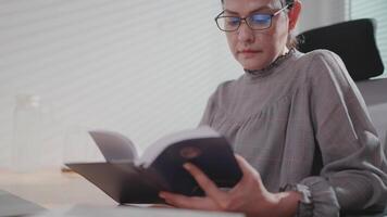 Close-up of a woman sitting at a table with the window open, drinking coffee and reading a book and enjoying the morning rainbow. video