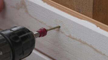 A man hands using a power tool fastens a board with a screw. Slow motion video