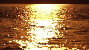 Blurred golden sea at sunset with shifting focus and bokeh effect. Sun reflects and sparkles on waves, illuminating golden sea. Holiday recreation concept. Abstract nautical summer ocean sunset nature video