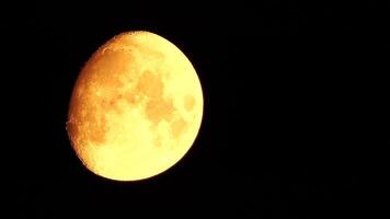 A glowing golden huge moon seen from earth through the atmosphere against a starry night sky. A large moon moves across the sky, the moon moving from the left frame to the right. video
