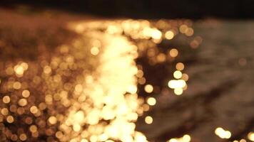 Abstract sea summer ocean sunset nature bokeh background. Small waves on azure water surface in motion blur with golden bokeh lights from sun. Holiday, vacation and recreational concept. Slow motion video