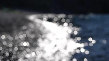 Abstract sea summer ocean sunset nature bokeh background. Small waves on azure water surface in motion blur with golden bokeh lights from sun. Holiday, vacation and recreational concept. Slow motion video