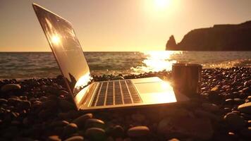 Silhouette of laptop and cup on the beach over sea sunset. Sparkling sea water on background. Freelancer, blogger working on notebook on the beach. video