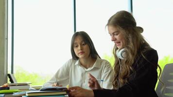 Two female students sitting by desk in lecture hall and discussing passage in book while one of them pointing at page video