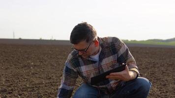 Senior farmer checks quality of soil before sowing. Farmer with a tablet in field holds earth in his hands. Agronomist checks the quality of sowing grain video