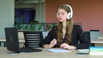 sorridente menina com fone de ouvido estudando on-line, usando computador portátil às universidade, levando notas, cópia de espaço video