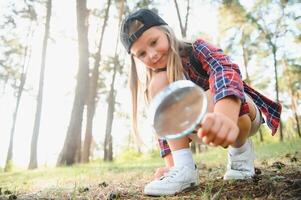 Rear view image of cute little girl exploring the nature with magnifying glass outdoor. Child playing in the forest with magnifying glass. photo