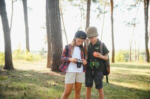 Two happy children having fun during forest hike on beautiful day in pine forest. Cute boy scout with binoculars during hiking in summer forest. Concepts of adventure, scouting and hiking tourism photo