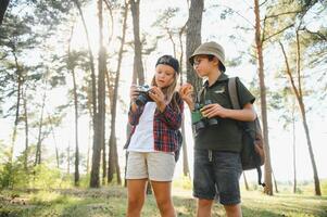 Group of curious happy school kids in casual clothes with backpacks exploring nature and forest together on sunny autumn day. photo