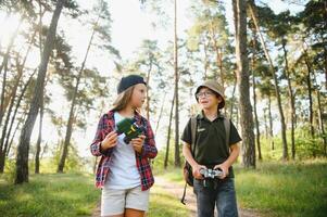 Happy excited school children with backpacks in casual clothes enjoying walk in forest on sunny autumn day, two active kids boy and girl running and playing together during camping trip in nature. photo