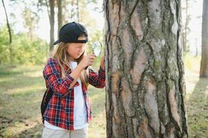 Image of cute kid with magnifying glass exploring the nature outdoors. Adorable little girl playing in the forest with magnifying glass. Curious child looking through magnifier on a sunny day in park. photo
