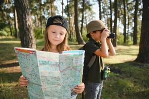 Two happy children having fun during forest hike on beautiful day in pine forest. Cute boy scout with binoculars during hiking in summer forest. Concepts of adventure, scouting and hiking tourism photo