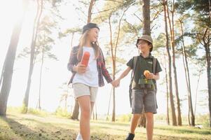 Happy excited school children with backpacks in casual clothes enjoying walk in forest on sunny autumn day, two active kids boy and girl running and playing together during camping trip in nature. photo