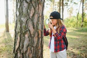Rear view image of cute little girl exploring the nature with magnifying glass outdoor. Child playing in the forest with magnifying glass. photo