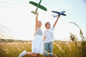 Running boy and girl holding two green and blue airplanes toy in the field during summer sunny day photo