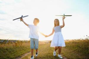 Running boy and girl holding two green and blue airplanes toy in the field during summer sunny day photo