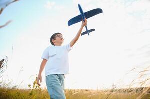 The kid runs with a toy plane. Son dreams of flying. Happy child, boy, runs on the sun playing with a toy airplane on the summer field photo